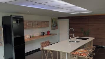 Une cuisine moderne avec un réfrigérateur noir, un îlot central blanc doté de tabourets de bar et un mur en bois.