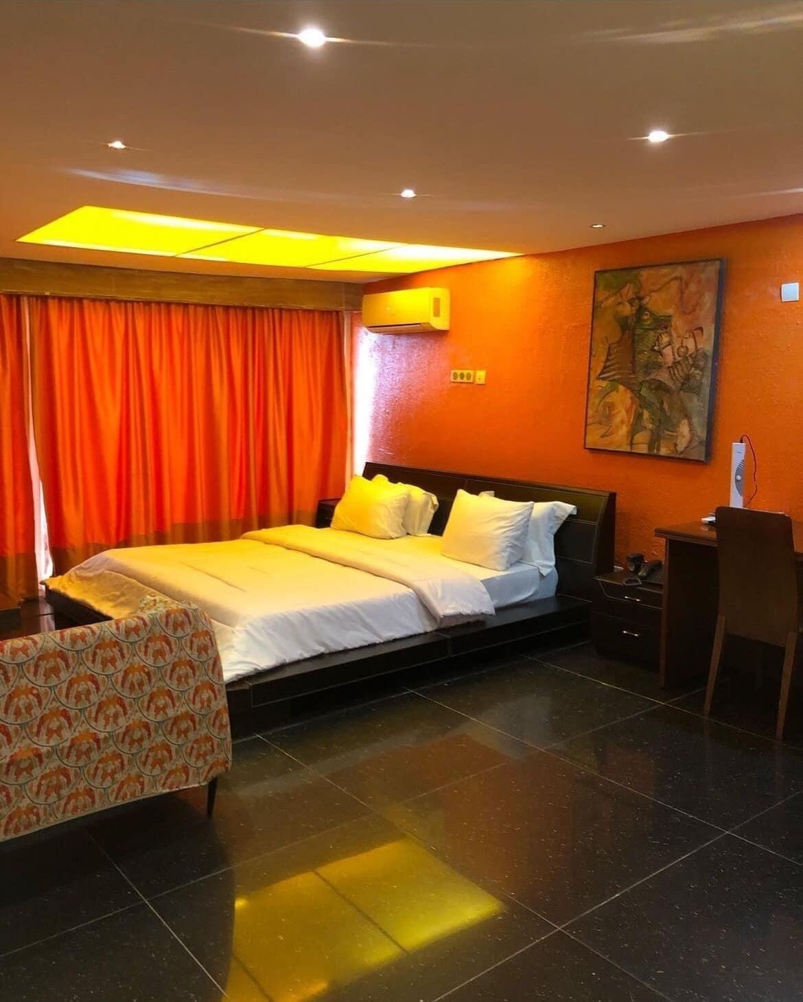 A hotel room with a large bed, a desk, a chair, and a painting on the wall.