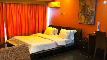 A hotel room with a large bed, a desk, a chair, and a painting on the wall.