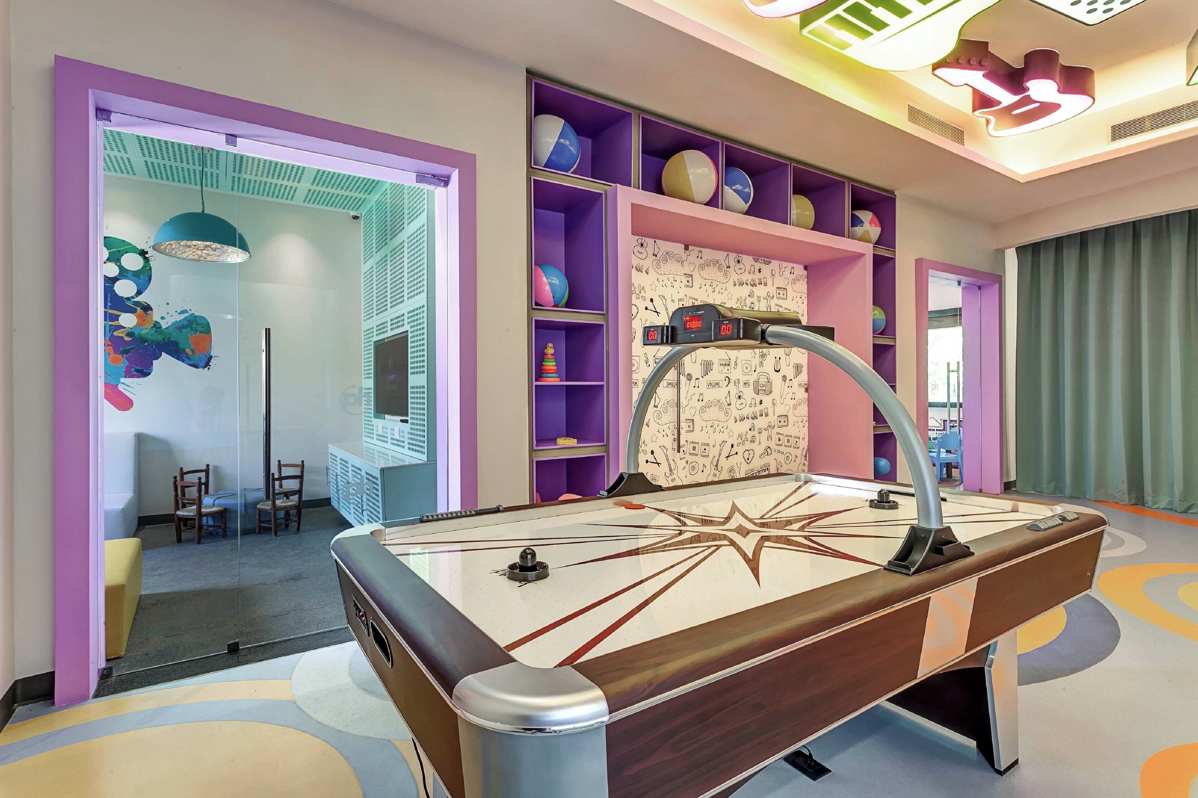 A pool table in a brightly colored room with shelves of sports balls and a wall with doodle patterns.
