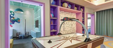 A pool table in a brightly colored room with shelves of sports balls and a wall with doodle patterns.