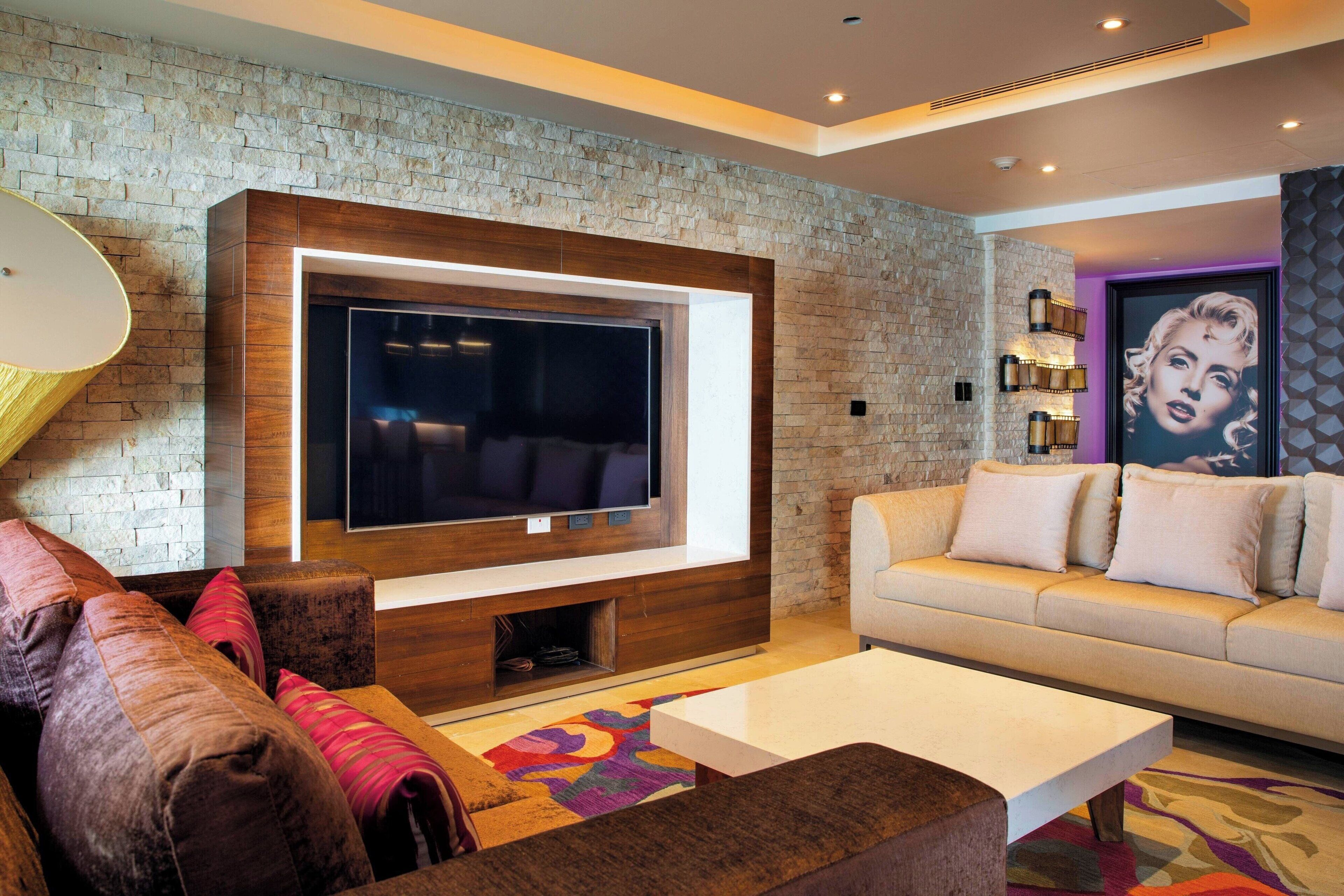 A modern living room with a large flat-screen TV mounted on a stone wall, a beige sofa, a coffee table, and a colorful rug.