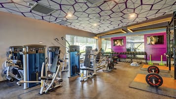 Ett gym med olika träningsmaskiner, utrustning för styrketräning och en lila vägg med konstverk.