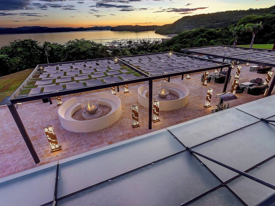 Une terrasse sur le toit offrant une vue sur un lac et des collines, avec un espace aménagé comprenant des tables et des chaises, ainsi qu’un foyer.
