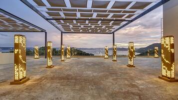Una terraza en la azotea con una pérgola, varios pilares iluminados y vistas a montañas distantes.
