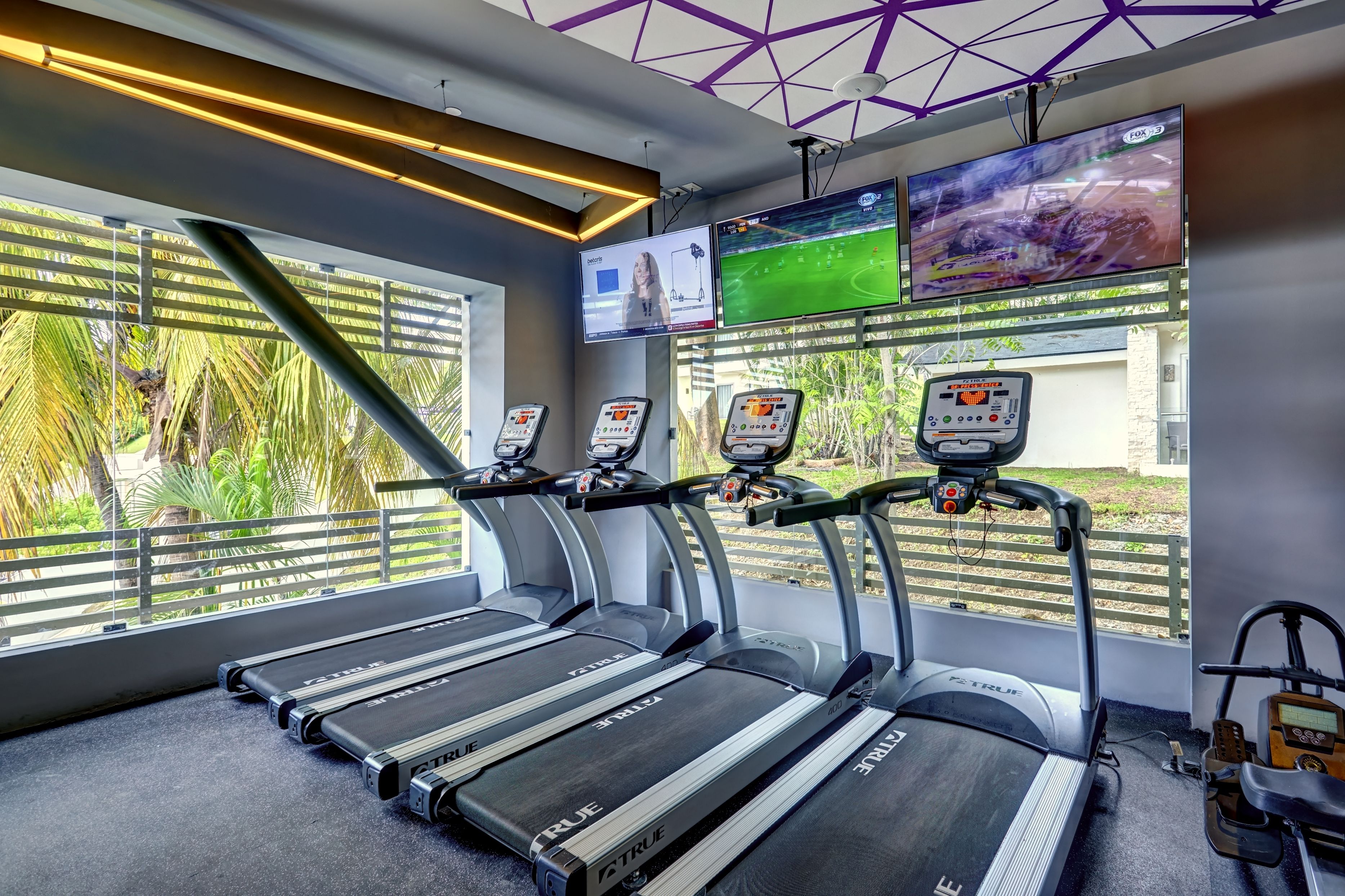 A gym with treadmills, exercise bikes, and a TV screen displaying a sports game.