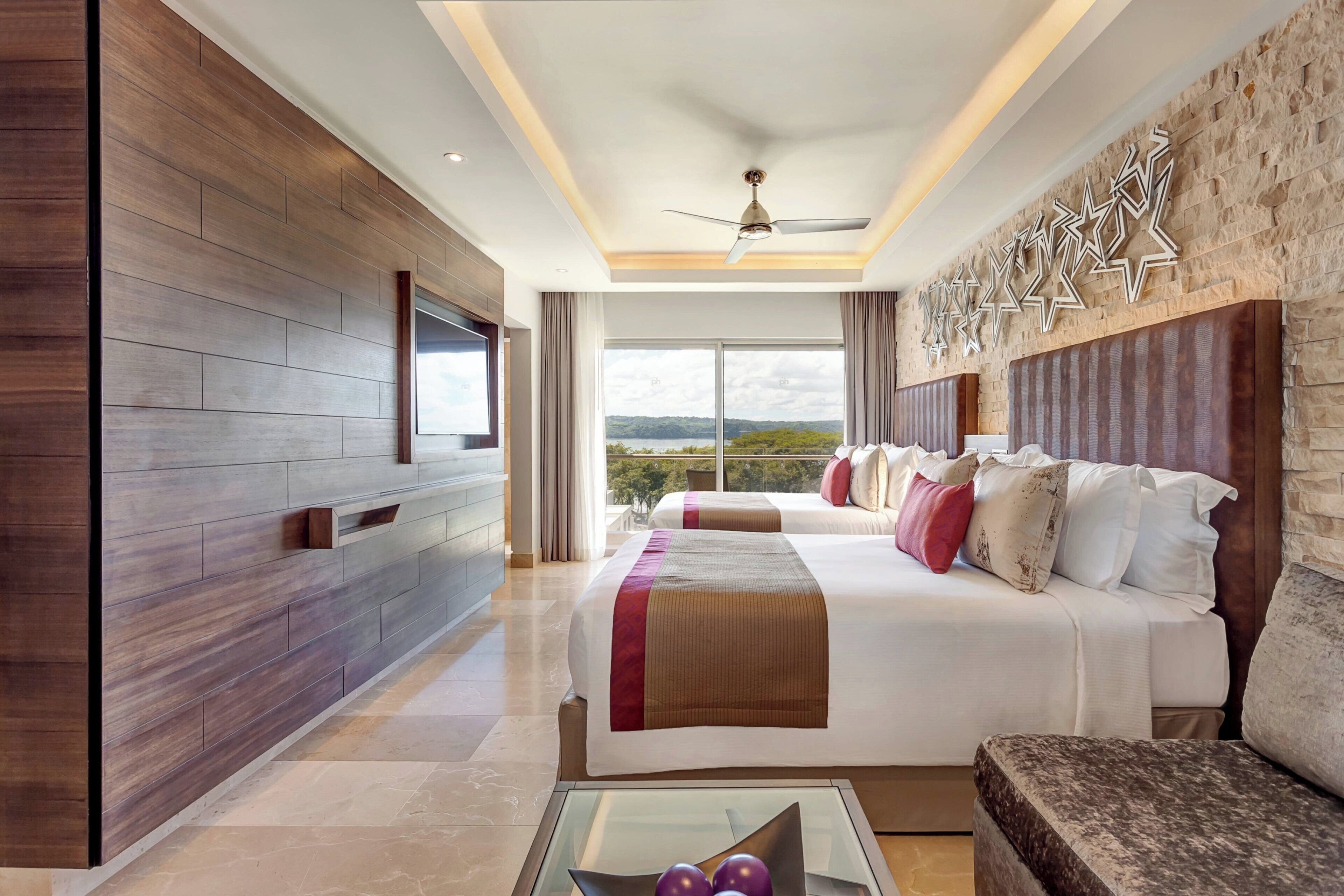 Habitación de hotel moderna con una cama grande, un sofá, una mesa de centro de vidrio y vistas al exterior.
