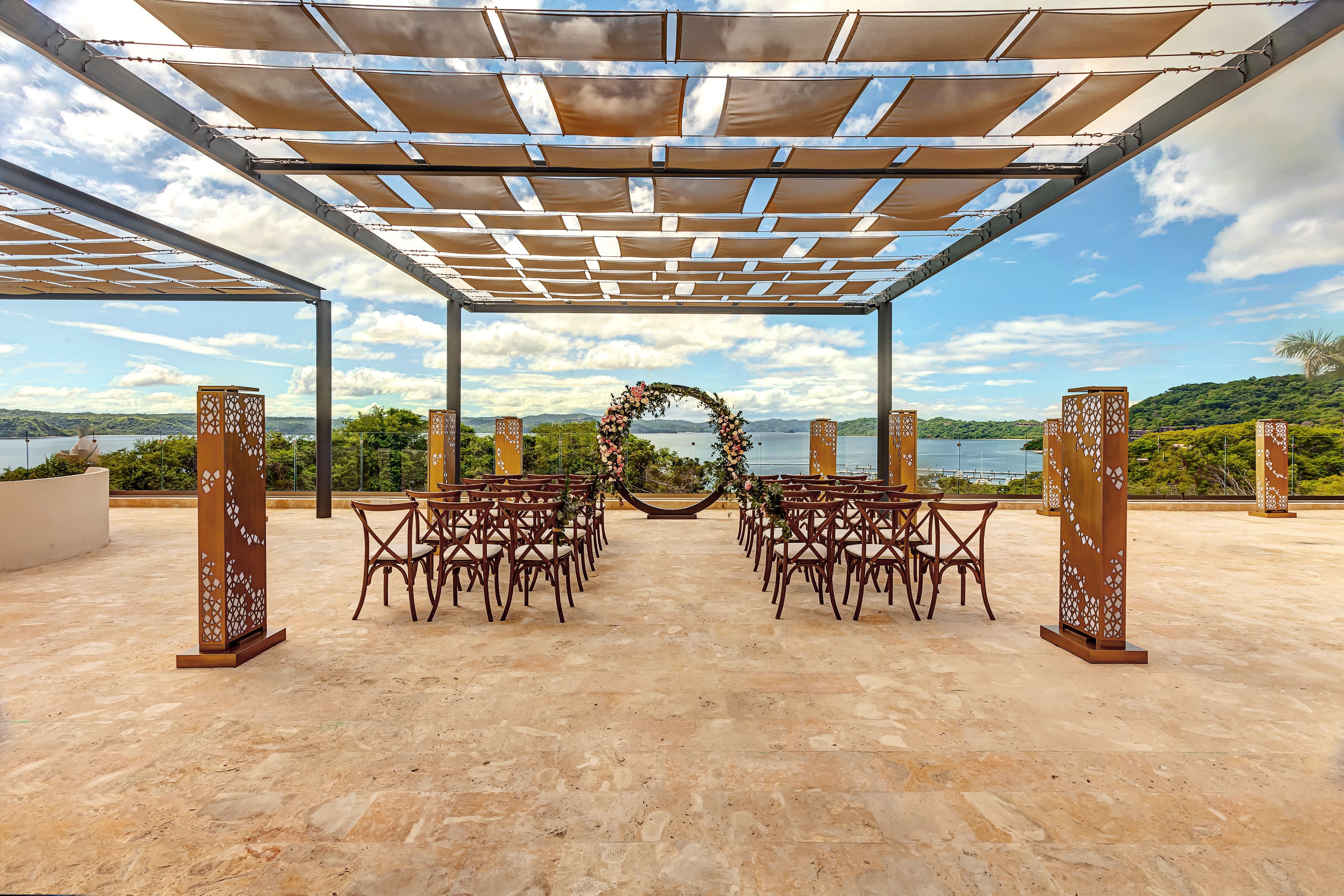 Decoração de casamento ao ar livre com pérgola, cadeiras e arco de flores.