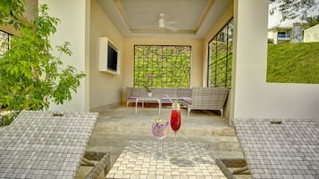 A sunlit patio with a table and chairs, a decorative screen, and a view of a hillside.