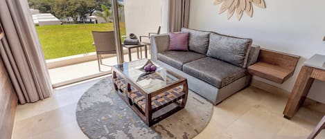 Un salon moderne avec une table basse en verre, un canapé gris et une vue sur l’extérieur.