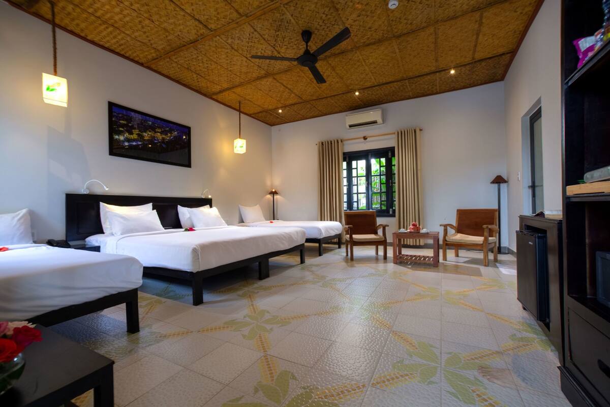 A hotel room with three beds, a ceiling fan, a large window with curtains, and a television.