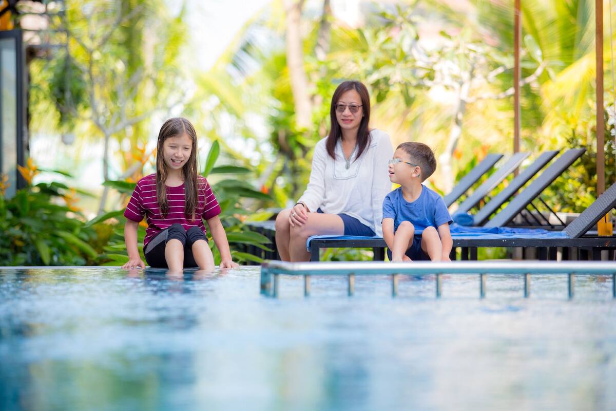 A poolside area with lounge chairs and a person sitting on the edge of the pool.
