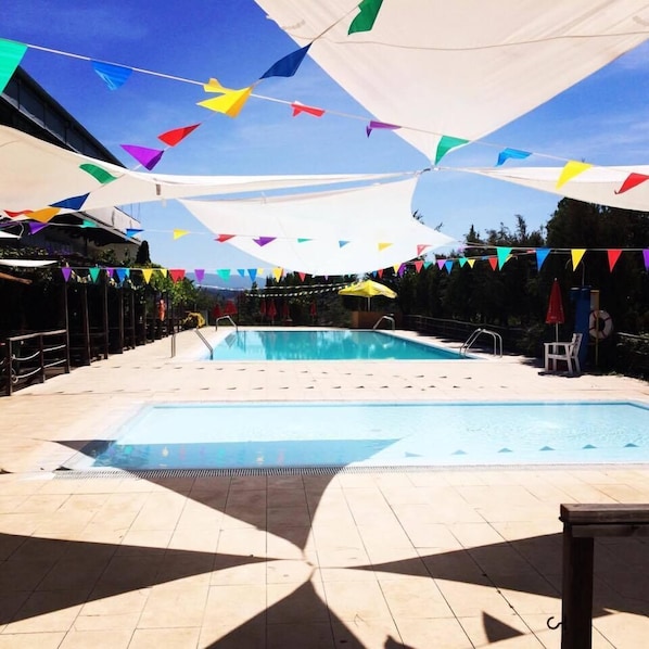 A swimming pool with a tiled deck, surrounded by colorful triangular flags and umbrellas.