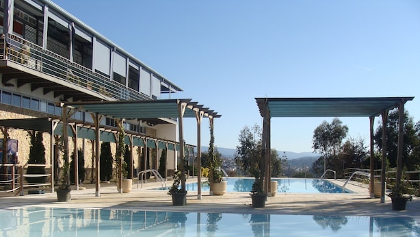 A pool area with a clear view of the pool, a covered seating area, and a building with multiple balconies. - Coimbra Camping & Bungalows (Coimbra)