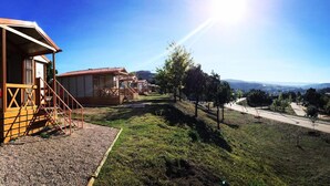 A row of wooden cabins with a gravel path leading to a road, surrounded by grassy areas and trees. - Coimbra Camping & Bungalows (Coimbra)