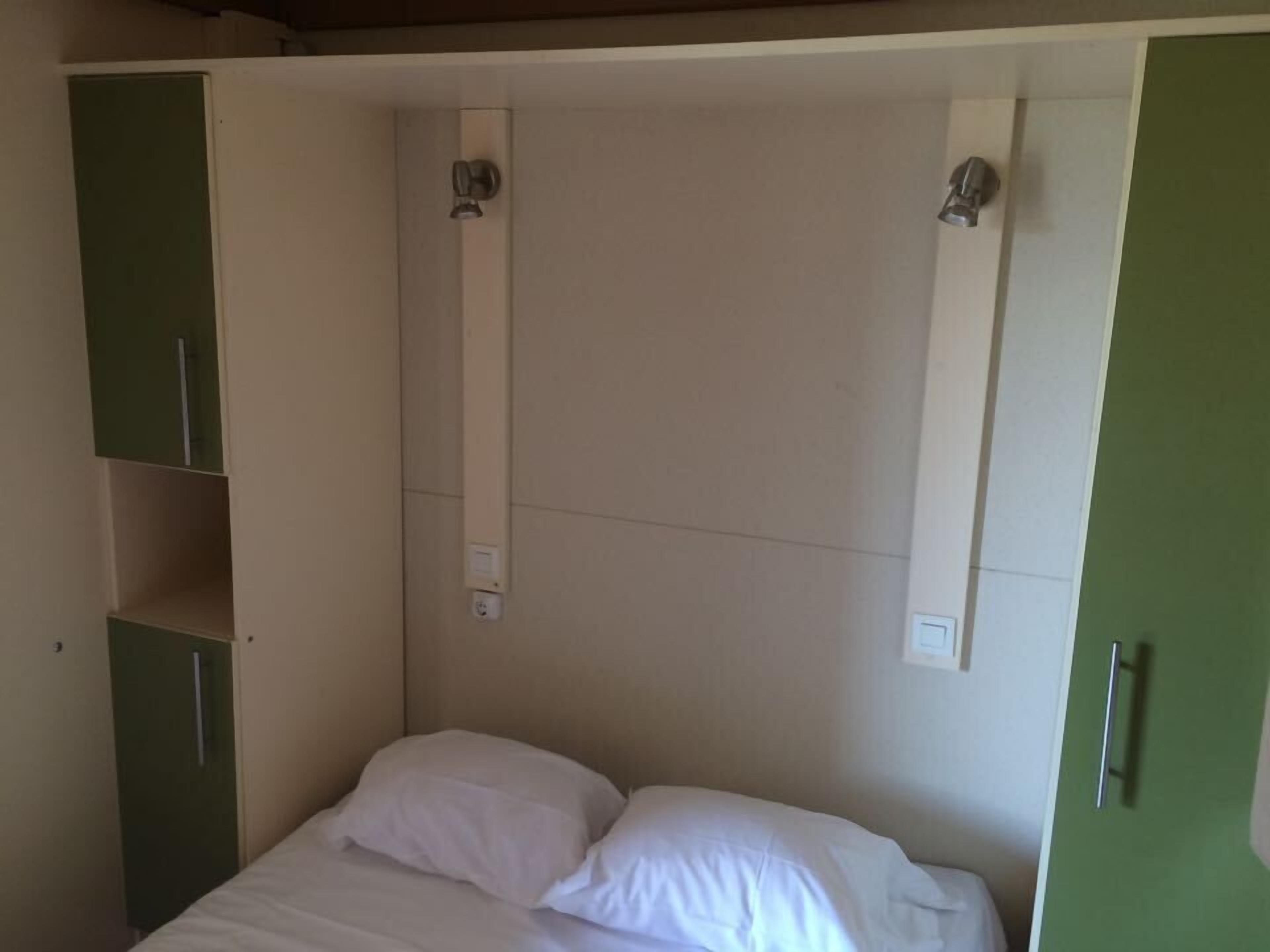A bedroom with a bed, white pillows, a green wardrobe, and a white ceiling with a light fixture.