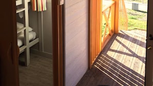 A room with a wooden deck, a view of the countryside, and a bunk bed with a striped curtain. - Coimbra Camping & Bungalows (Coimbra)