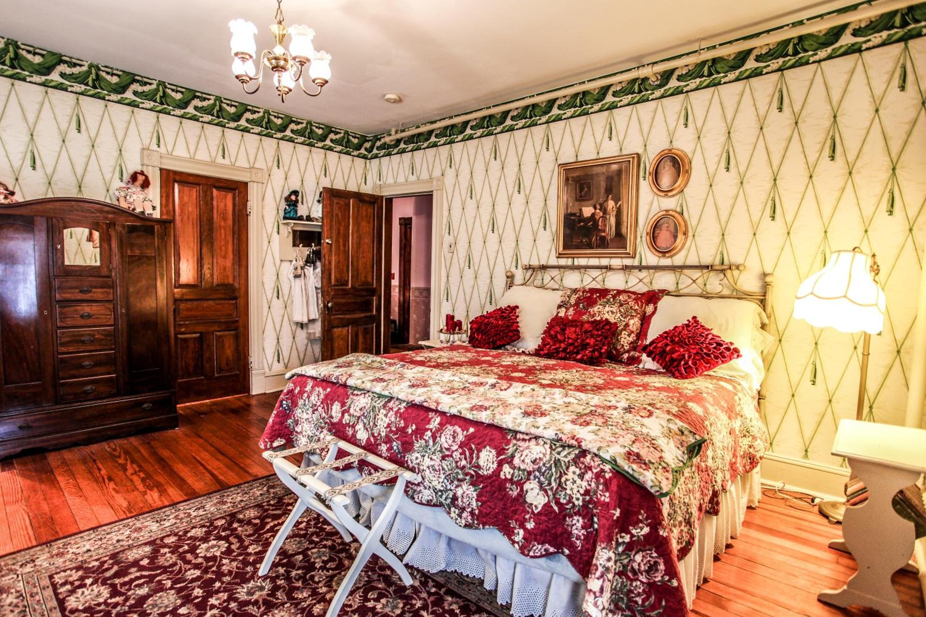 A bedroom with a large bed, wooden wardrobe, and a chandelier.