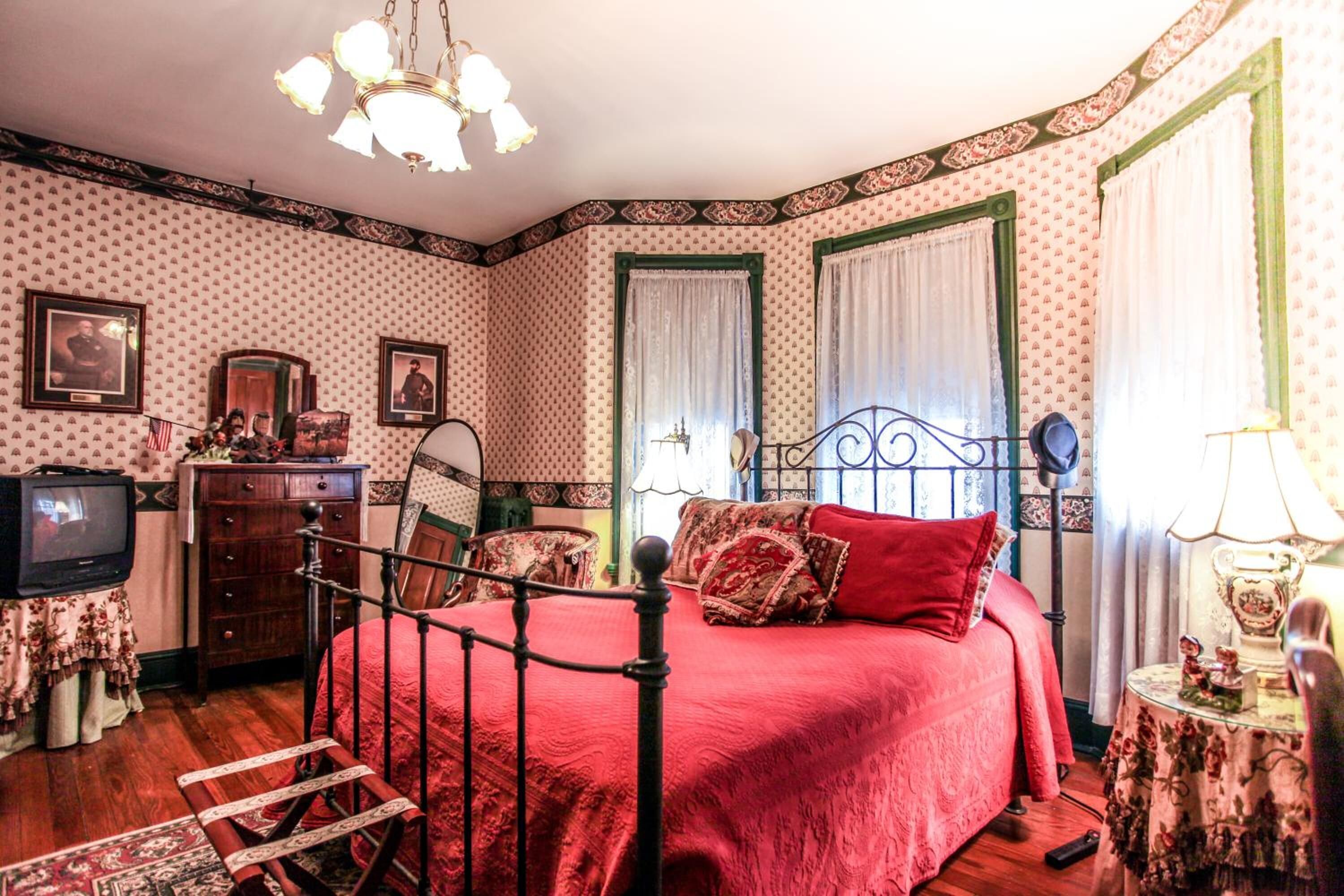 A bedroom with a four-poster bed, a dresser, a television, and patterned wallpaper.