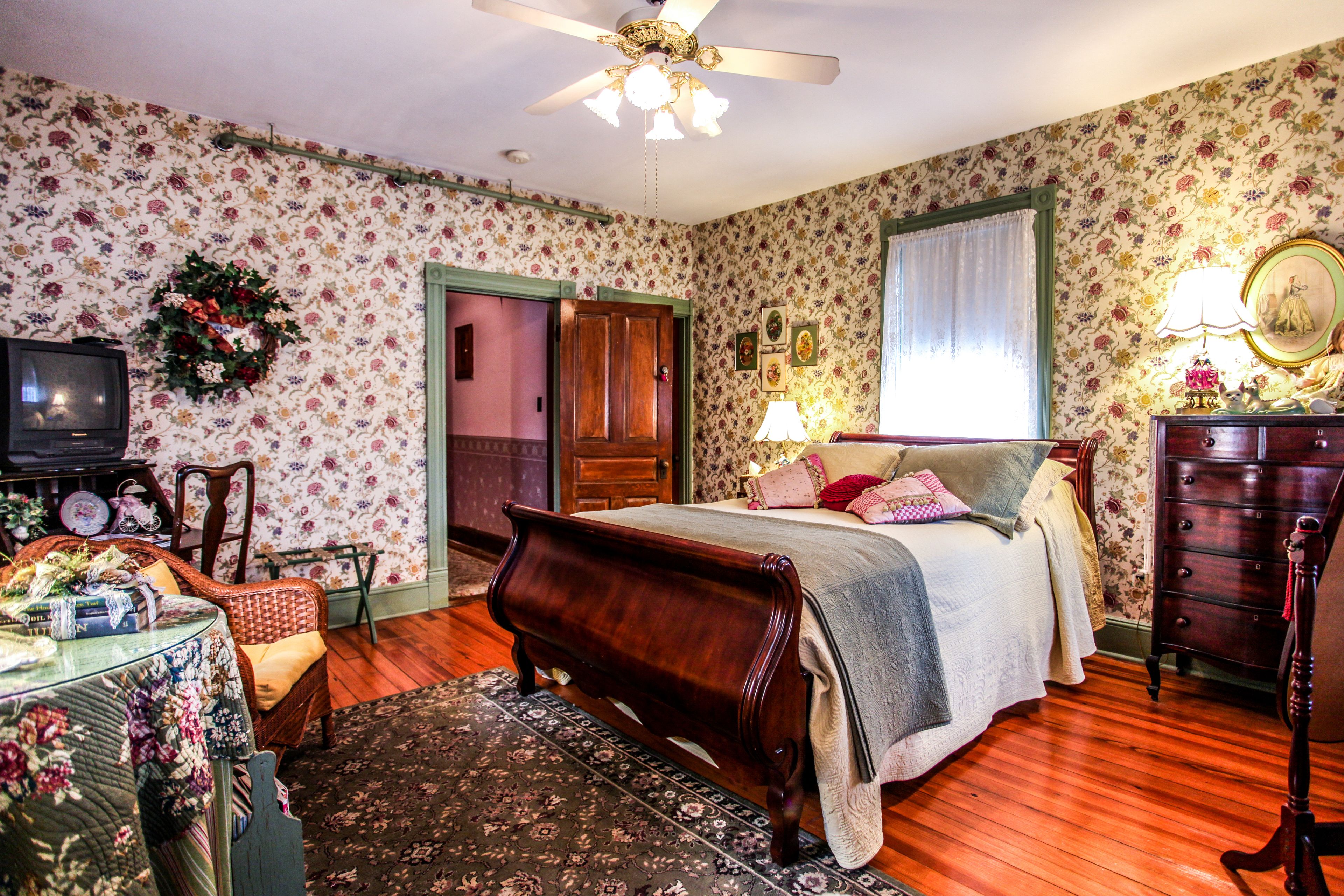 Un dormitorio con cama de madera, televisor, cómoda y papel tapiz con motivos florales.