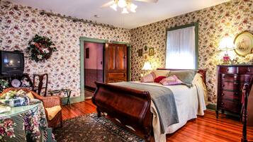 Un dormitorio con cama de madera, televisor, cómoda y papel tapiz con motivos florales.