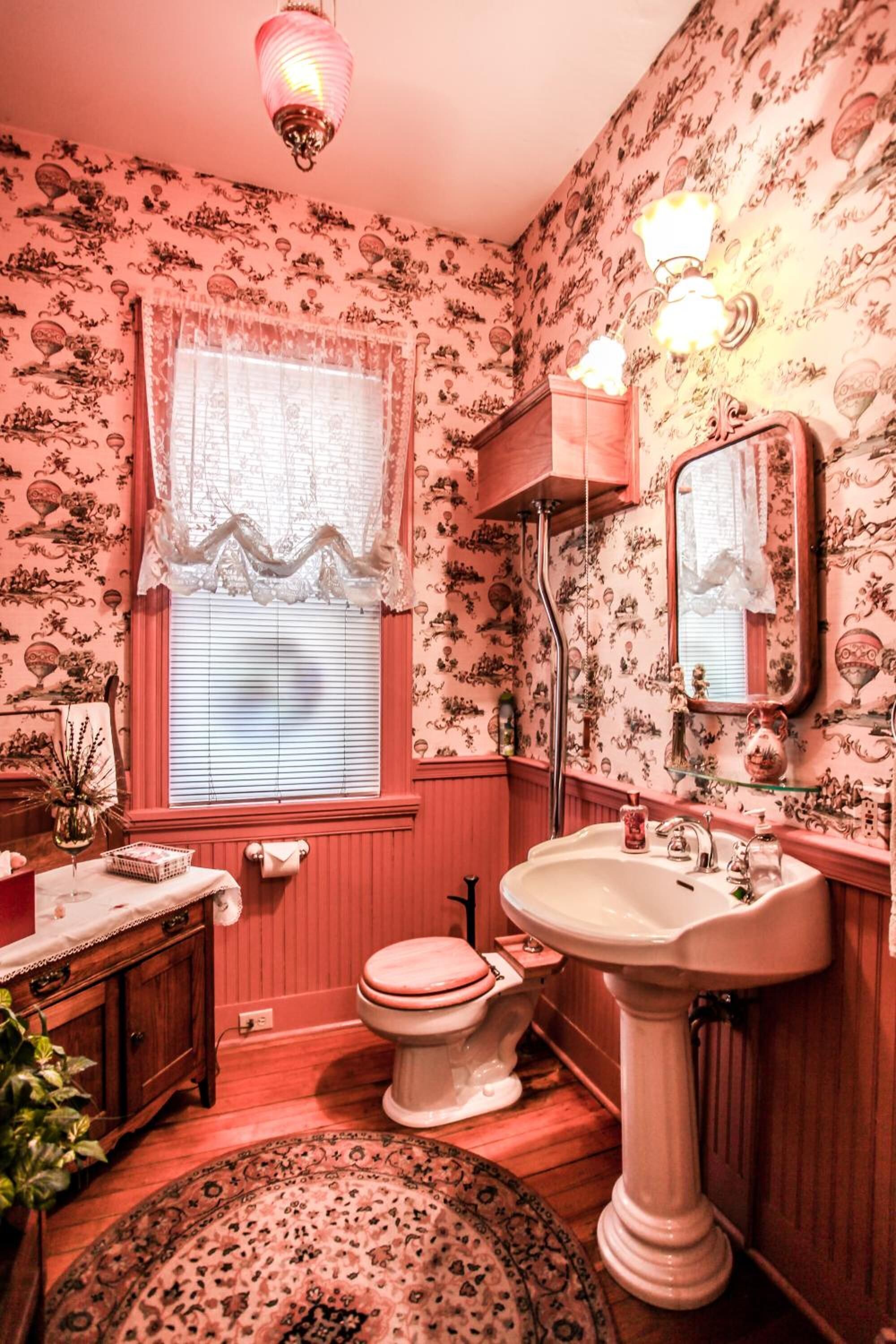 Un baño de diseño vintage, con un tocador de madera, un lavamanos pedestal y un inodoro.