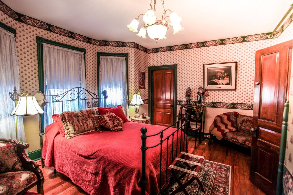 A bedroom with a four-poster bed, a wooden chair, a small table, and a door.
