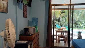 A room with a bed, a desk, a fan, a water dispenser, and a television on the wall.