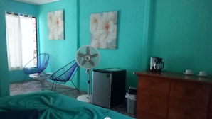 A room with teal walls, a bed, a fan, a coffee maker, and a dresser.