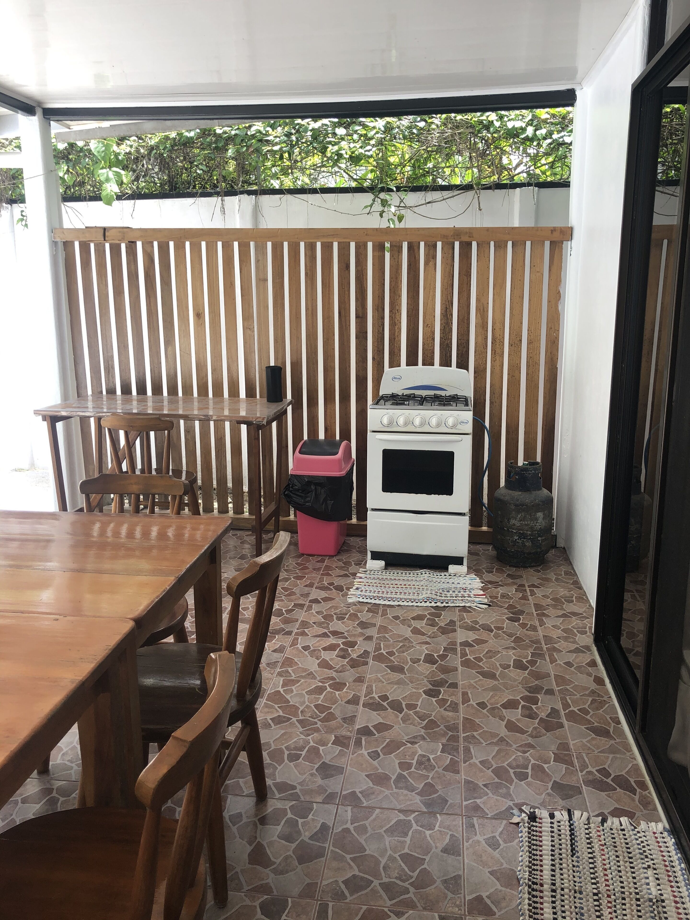 Un'area patio con tavolo e sedie di legno, un fornello a gas, un cestino e una bombola di gas.