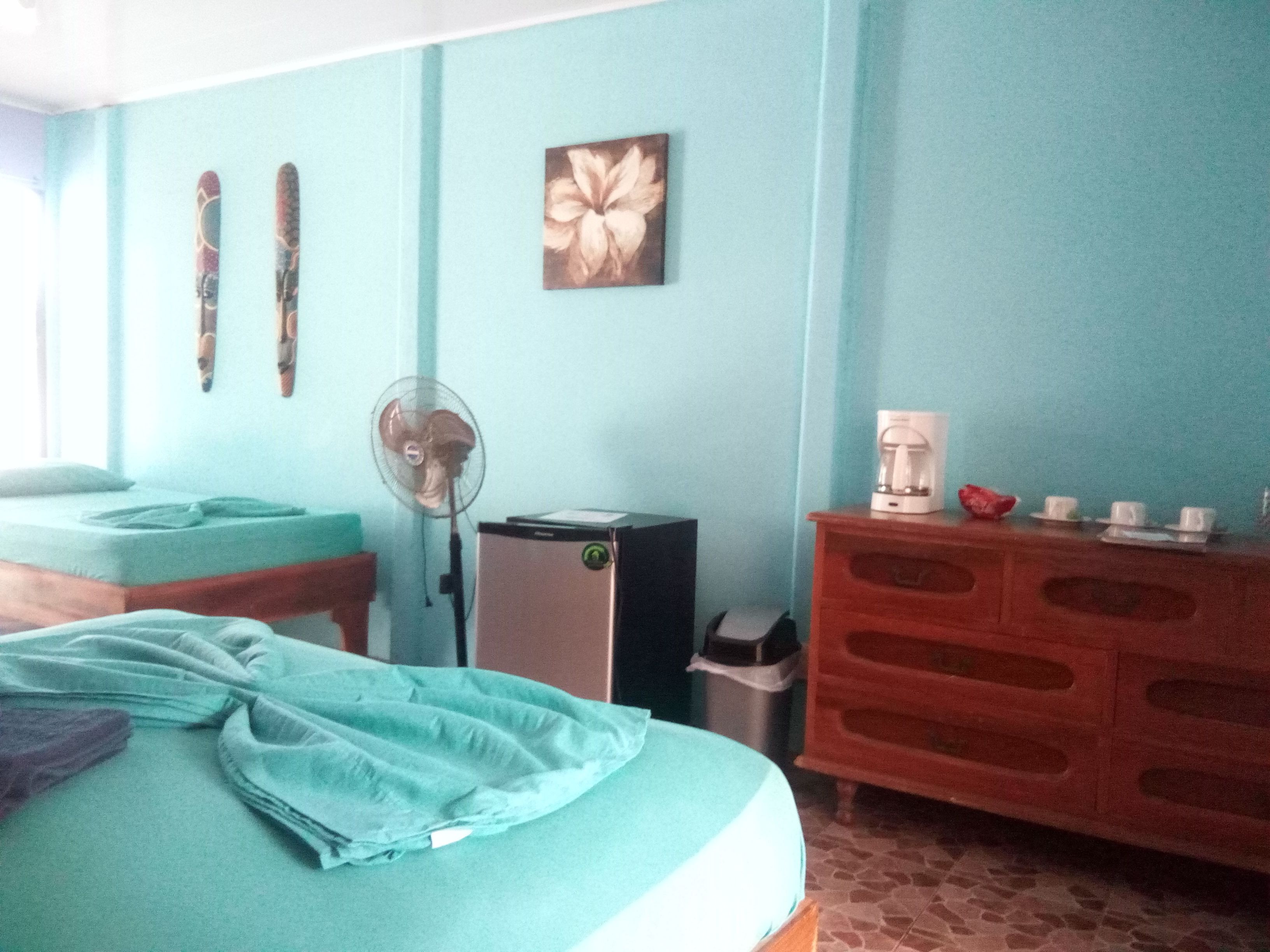 A room with a bed, a dresser, a fan, and a coffee maker.