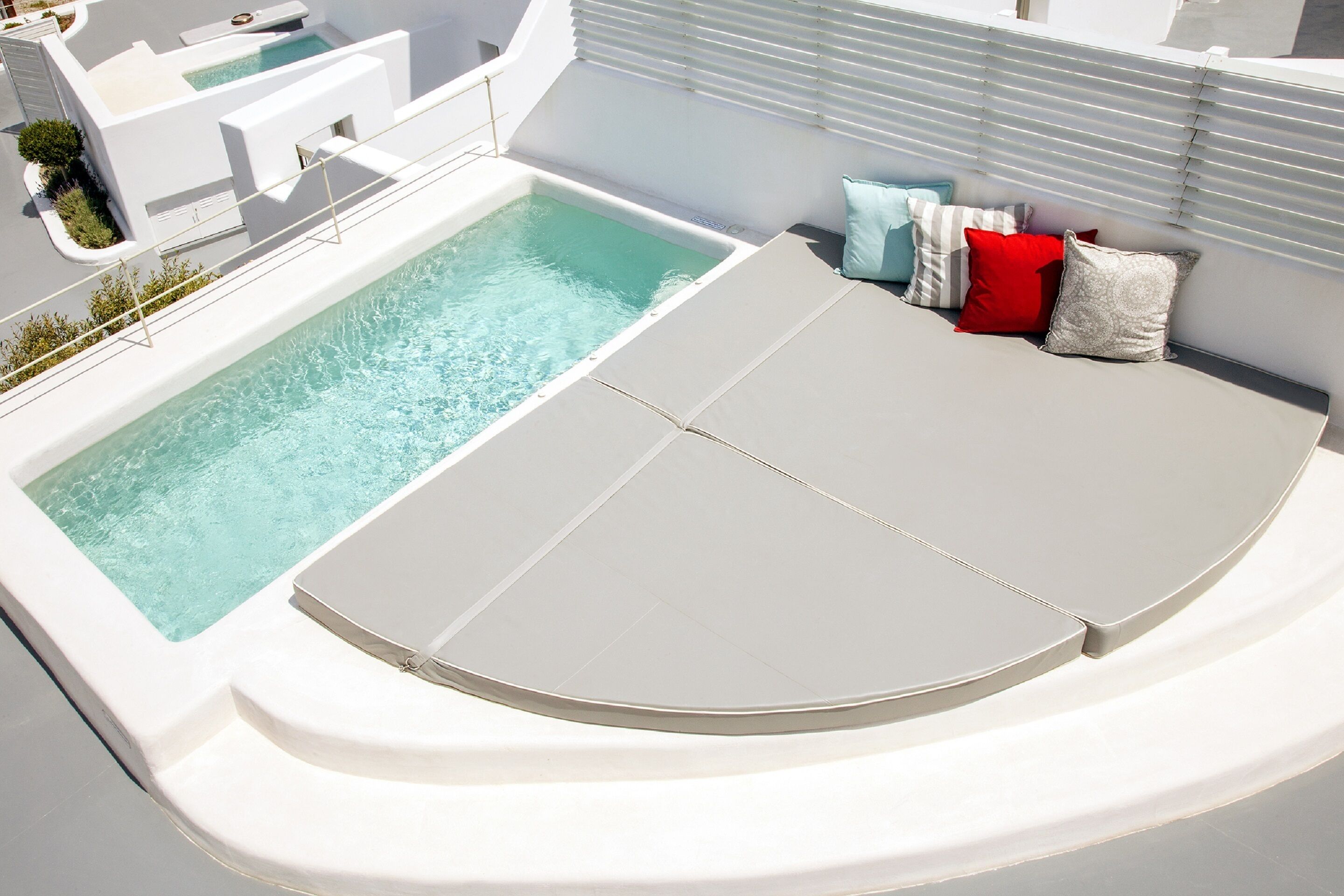 A rooftop pool area with a sun lounger and a variety of pillows.