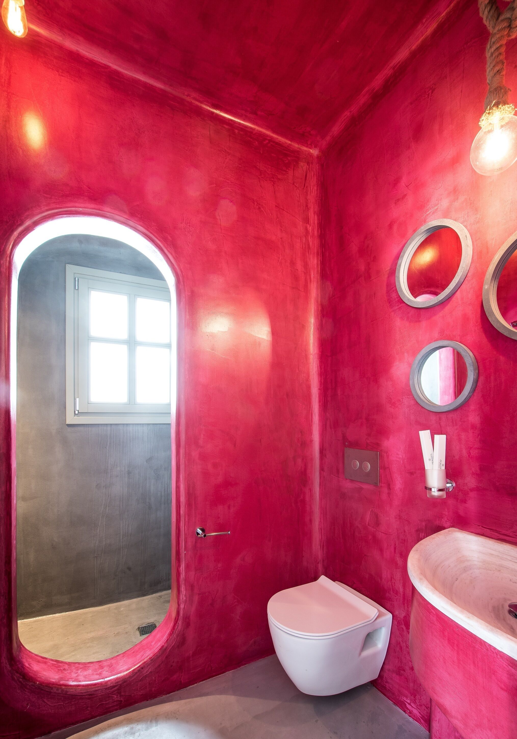 A bathroom with a red wall, a white toilet, a sink, and two mirrors.