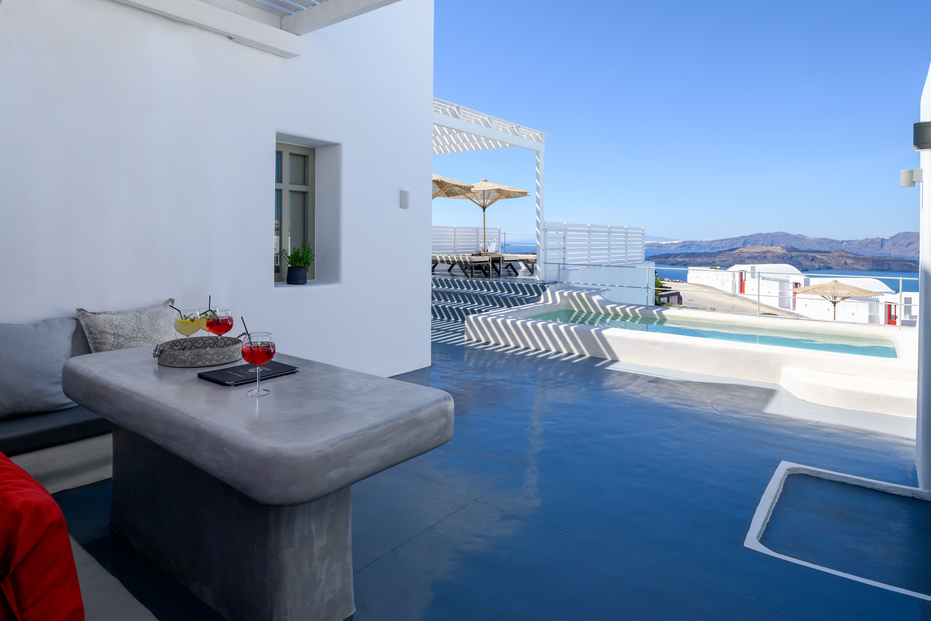 A modern outdoor seating area with a pool, a view of the sea, and a clear sky.