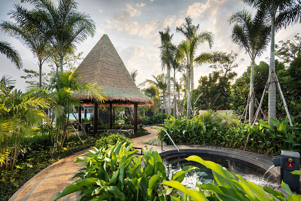 A thatched-roof structure surrounded by lush greenery and a small water feature.
