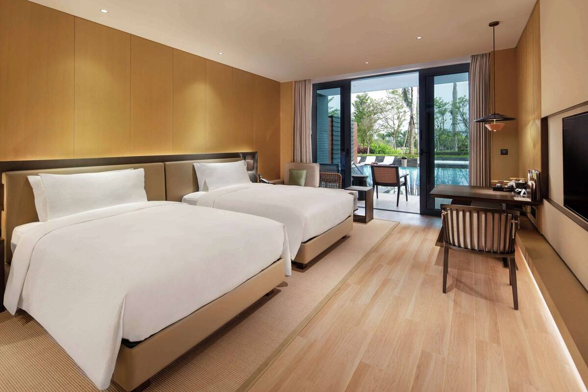 A hotel room with two beds, a desk, a chair, and a TV.