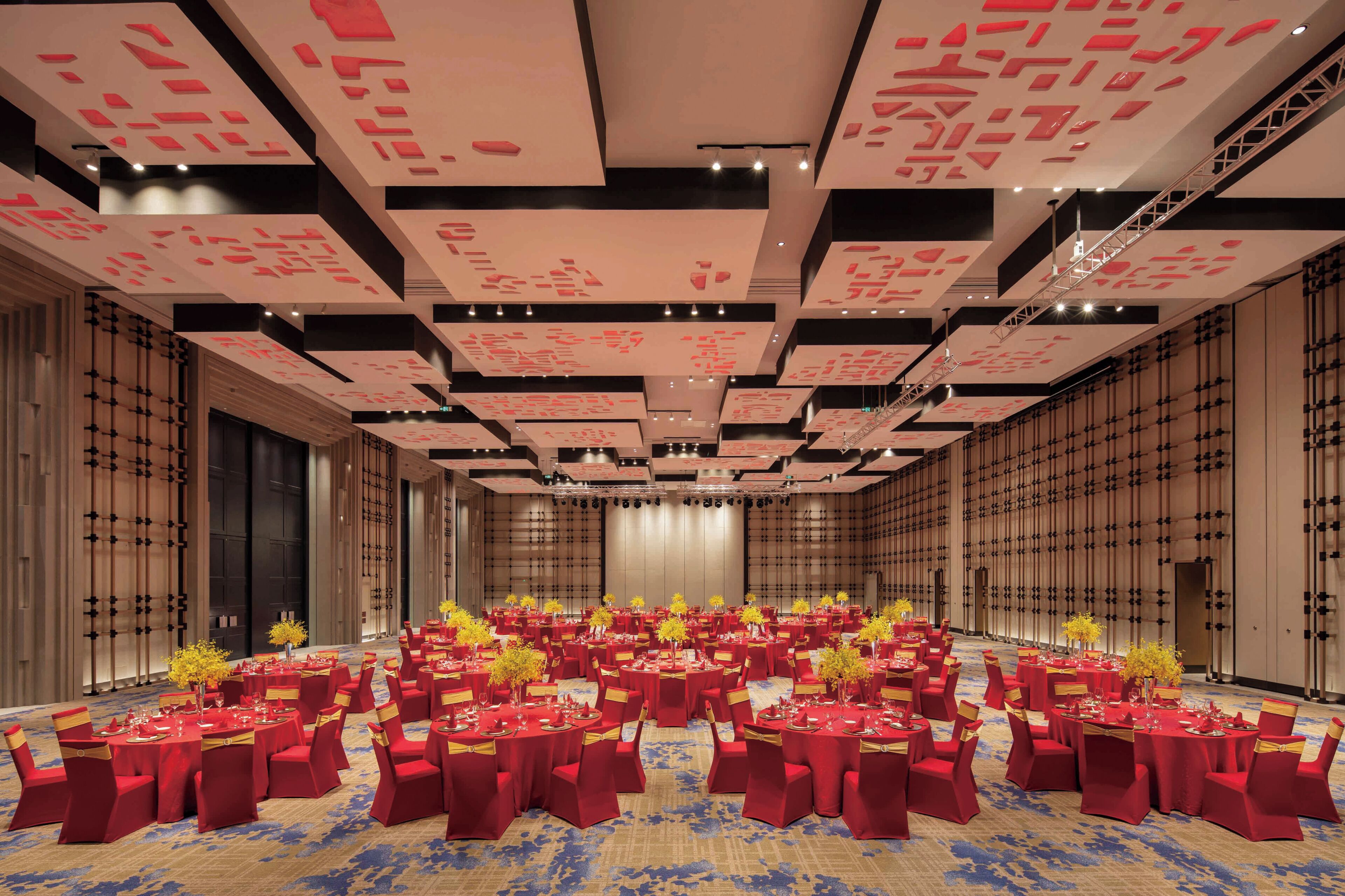 Un amplio salón de conferencias con varias mesas redondas, sillas rojas y una alfombra estampada.