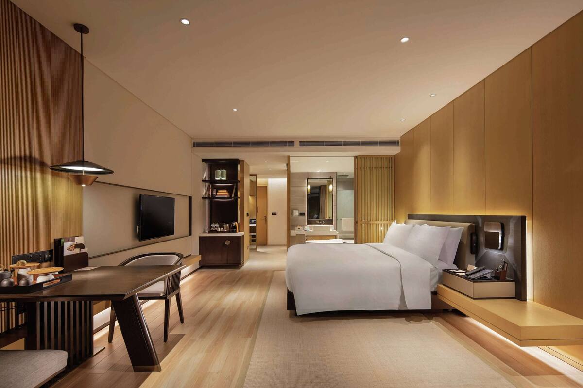 A modern hotel room with a large bed, a desk, and a television.