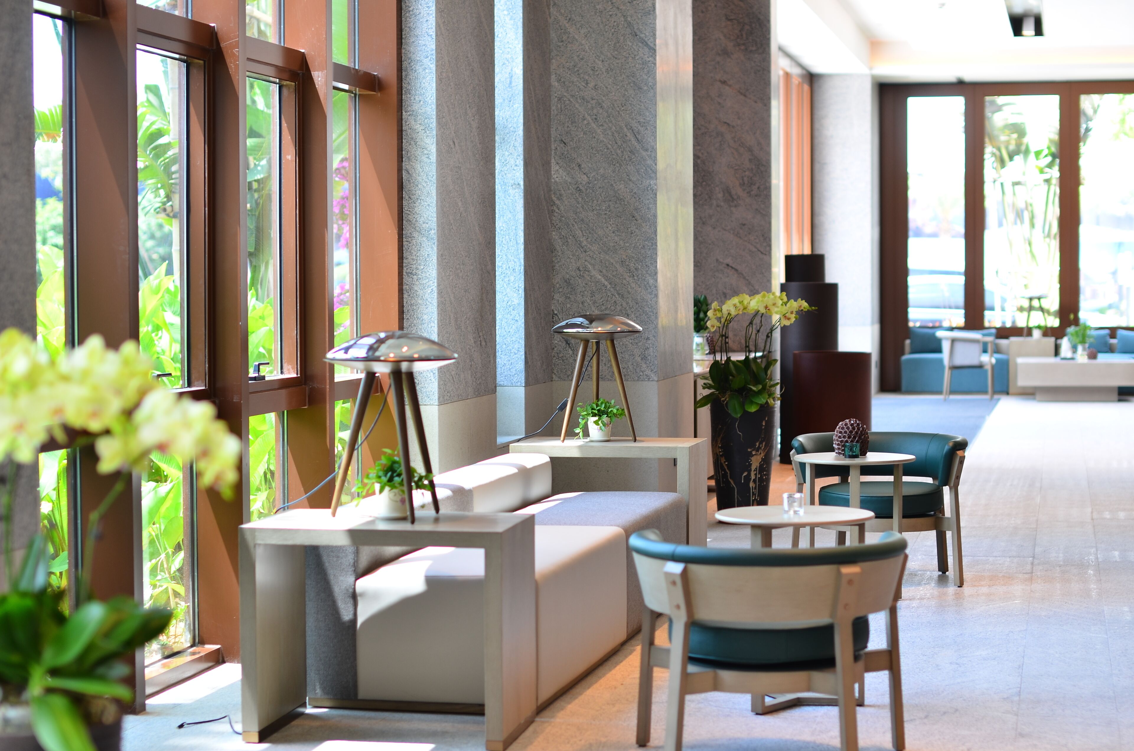 A modern lobby with seating areas, a reception desk, and large windows with greenery outside.