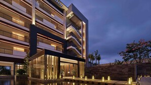 Un hotel moderno con varios pisos, una piscina reflectante e iluminación exterior.