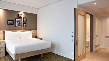 Quarto de hotel moderno com uma cama, mesas de cabeceira e luminária fixada na parede.