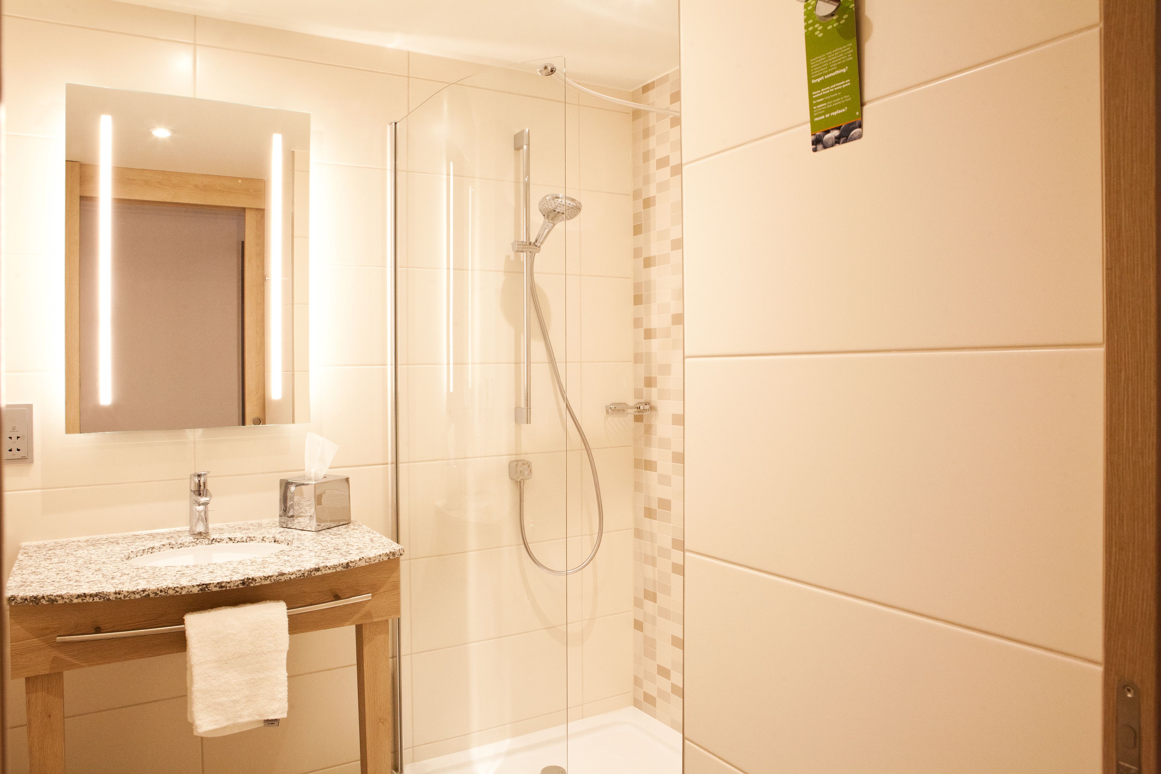 A modern bathroom with a granite countertop sink, a mirror, a handheld showerhead, and a glass-enclosed shower.
