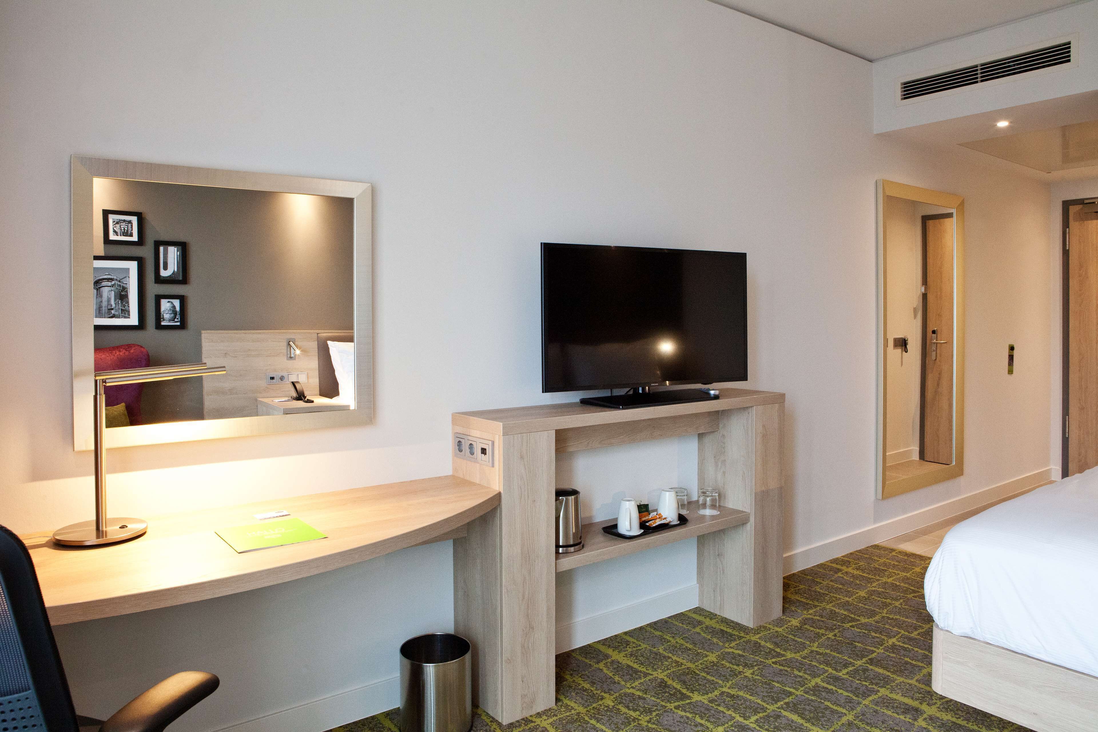 Hotelkamer met een bed, bureau met televisie, spiegel en klein kastje met bekers en waterkoker.
