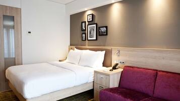 A hotel room with a bed, a nightstand, a phone, and a red sofa.