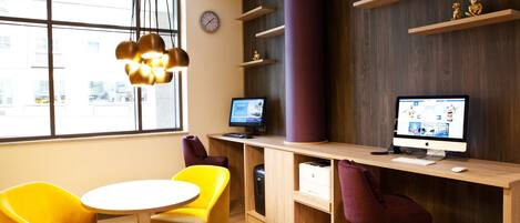 A modern office space with two desks, two chairs, a round table, a purple rug, and a large window with a view of the city.