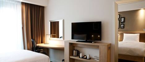 Une chambre d’hôtel avec deux lits, un bureau avec une télévision, une machine à café et un miroir.