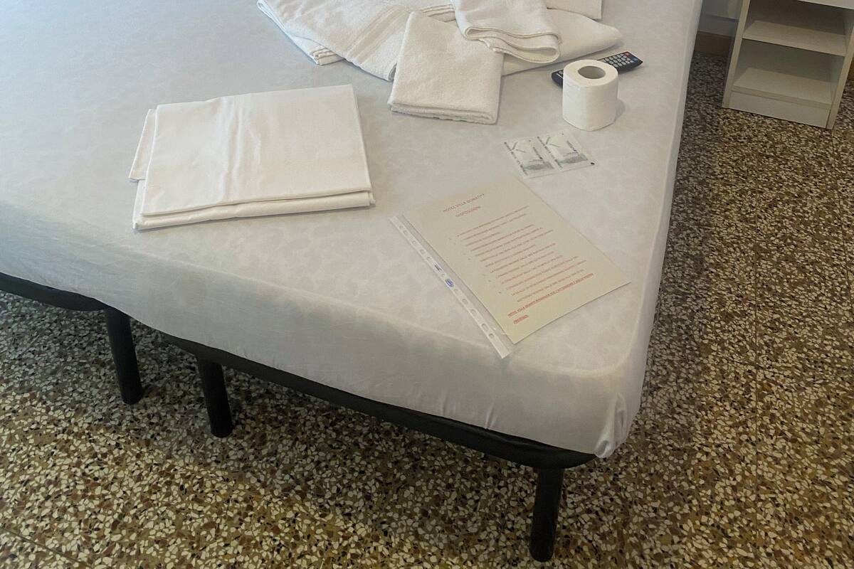 A neatly made bed with pillows, folded towels, a remote control, a tissue roll, and a menu on the bedside table.