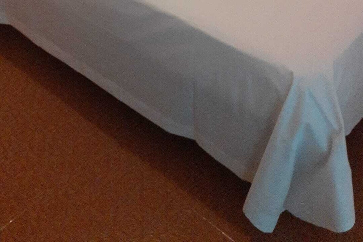 A hotel room with two beds, each with white linens and pillows. There is a folded towel on the bed, and a telephone mounted on the wall.