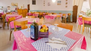 A dining area with tables covered in pink and blue checkered tablecloths, wooden chairs, and a bottle of olive oil on one table. - Hotel Villa Donati (Rimini)