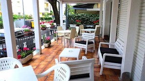 An outdoor patio with white furniture, potted plants, and a view of the street. - Hotel Villa Donati (Rimini)